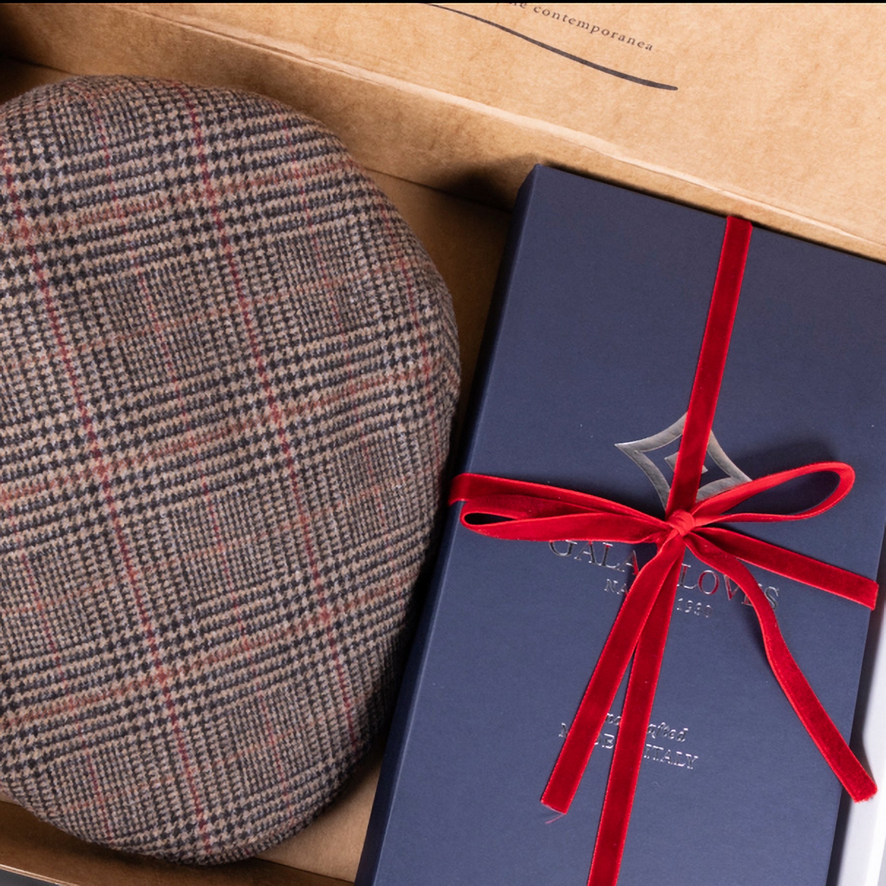 Checkered wool cap resting beside a luxurious gift box, elegantly tied with a red ribbon, showcasing Gala Gloves branding.