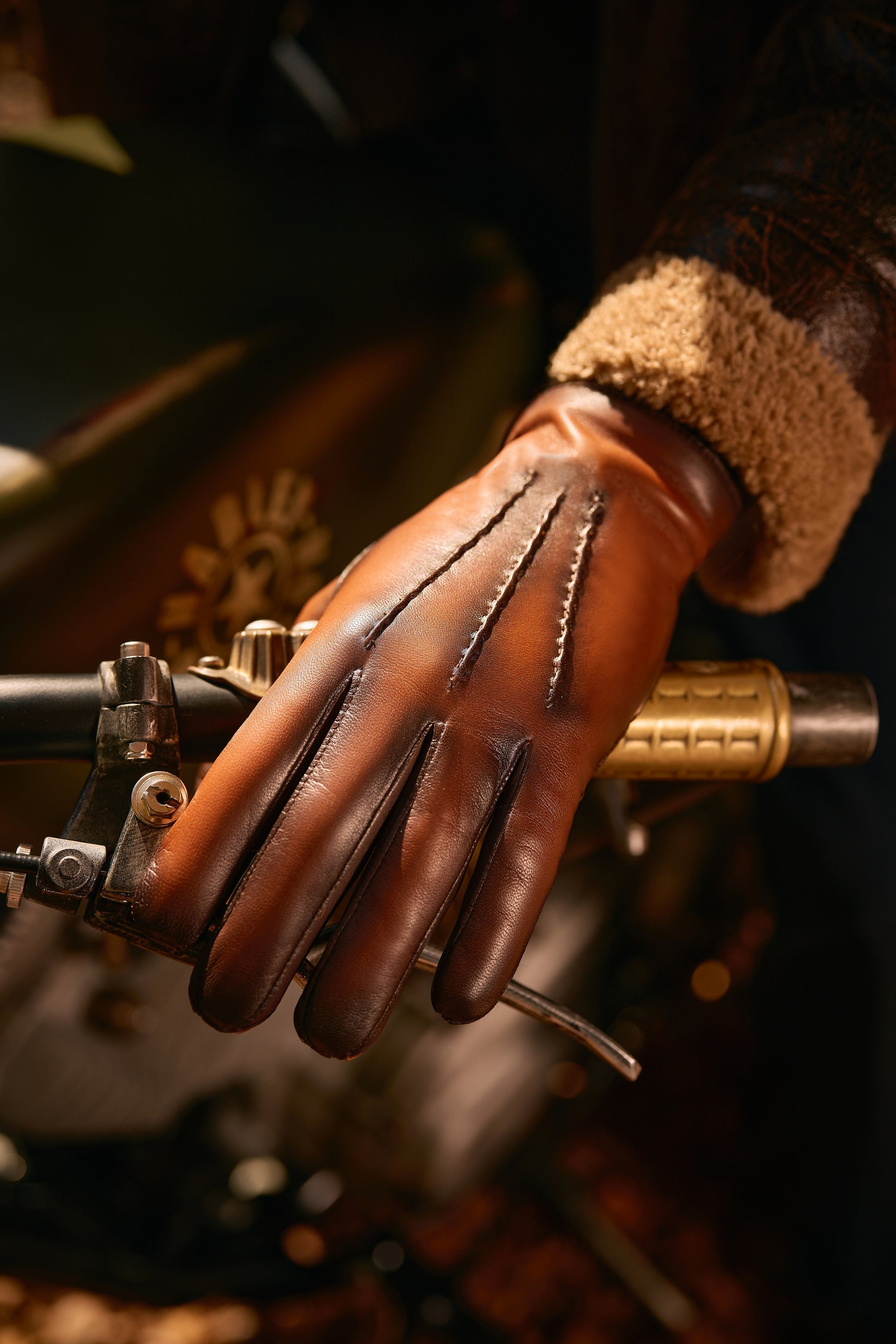 Men's vintage-style brown leather gloves with elegant stitching, resting on a motorcycle handlebar, showcasing Italian craftsmanship.