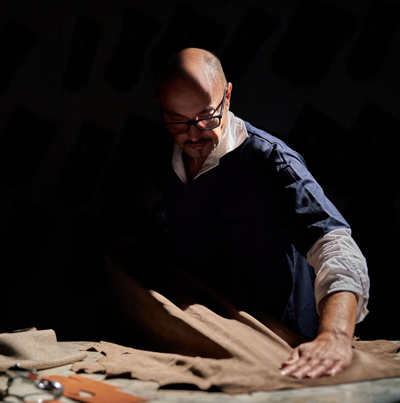 Alessandro Pellone carefully inspecting soft brown leather, showcasing meticulous attention to detail in Italian glove craftsmanship.