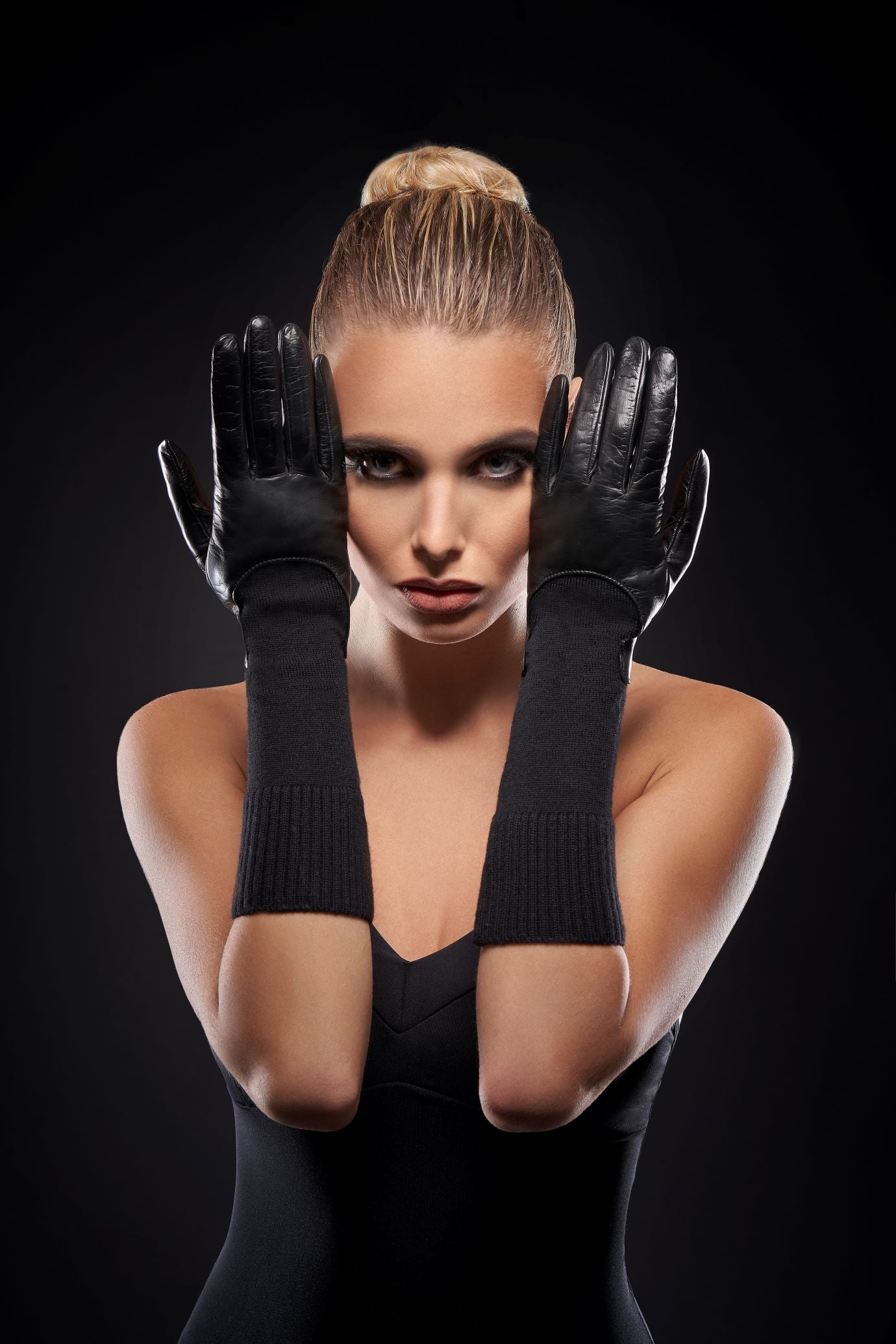 Model wearing Women's unlined black sheepskin gloves with medium-length wool sleeves, elegantly showcased against a dark backdrop.
