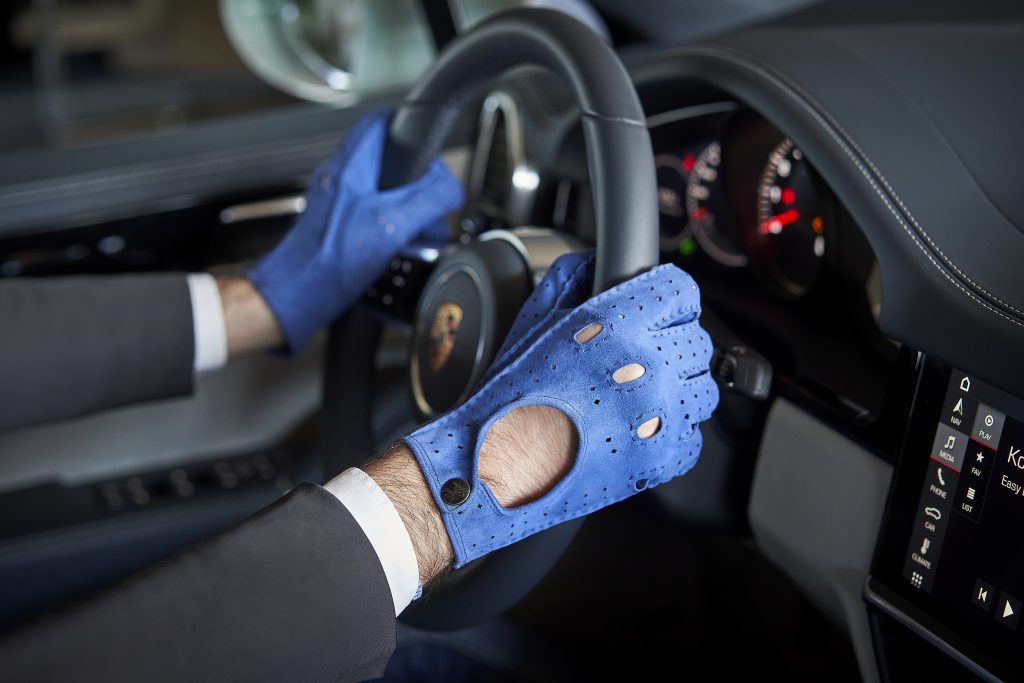 Driver wearing blue perforated leather driving gloves gripping steering wheel in luxury sports car - Gala Gloves performance style