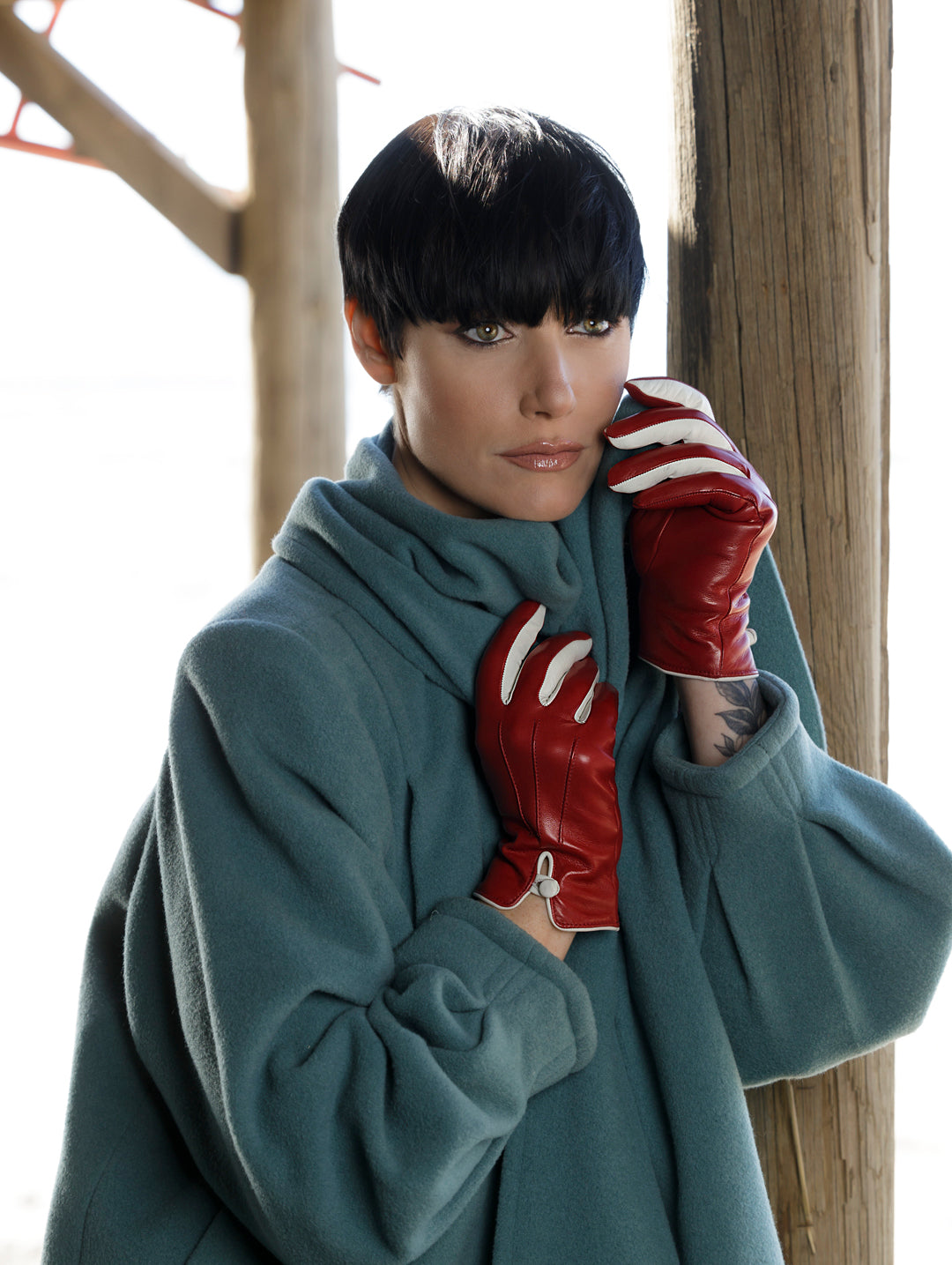Model wearing red nappa leather gloves with white accents, styled elegantly against a soft teal coat in natural light.